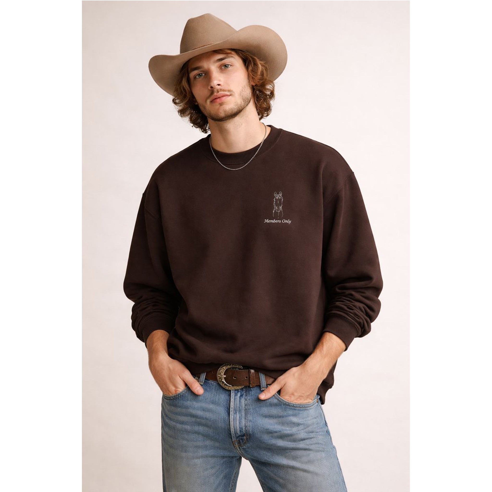 Man wearing a brown sweatshirt with a logo, blue jeans, and a cowboy hat on a plain background