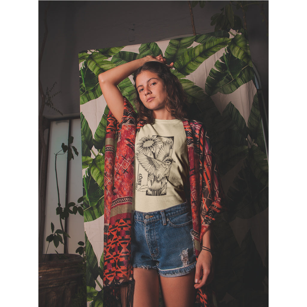 Person wearing a graphic t-shirt and colorful jacket in front of a leafy background – Bamerix