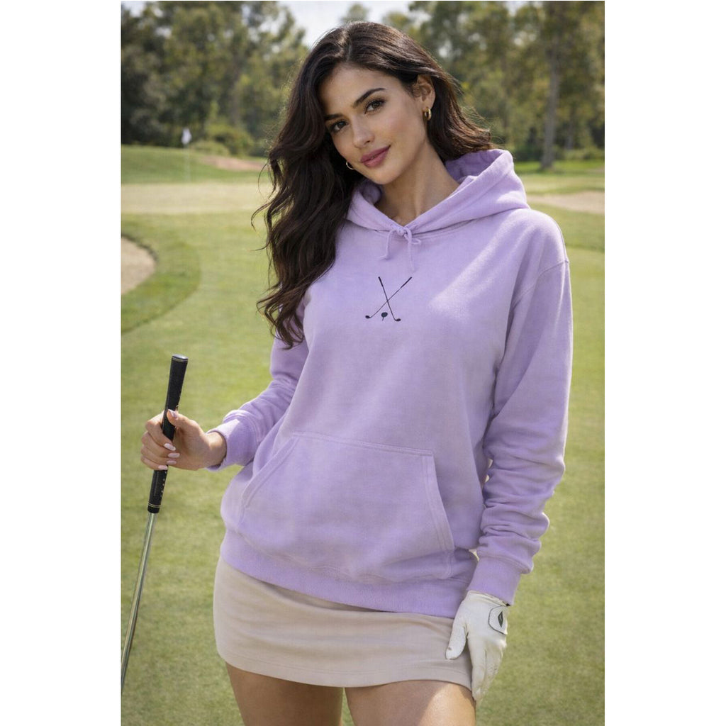 Woman in a purple hoodie and beige skirt holding a golf club on a golf course