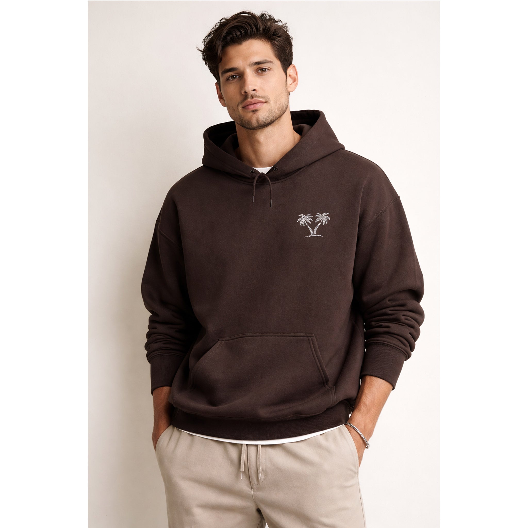 Man wearing a brown hoodie with a palm tree logo against a plain background