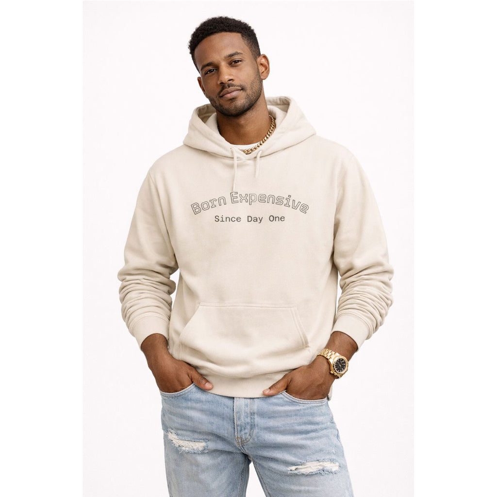 Man wearing a beige hoodie with text and light blue jeans on a white background