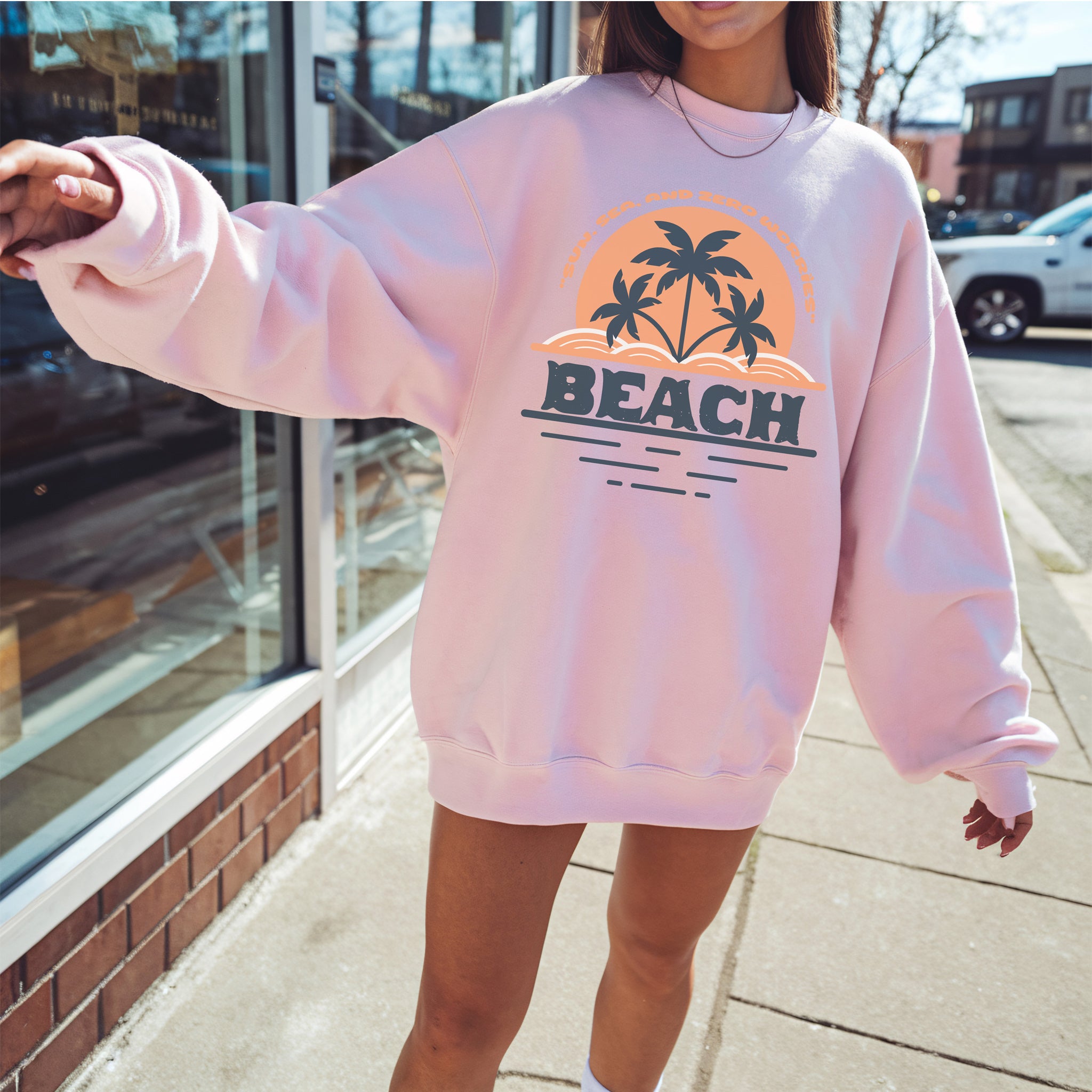 Person wearing a pink sweatshirt with 'BEACH' and palm tree design on a sidewalk.