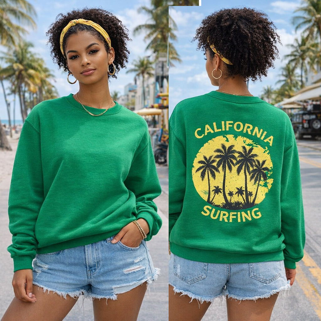 Woman wearing a green sweatshirt with 'California Surfing' design, standing on a beach.