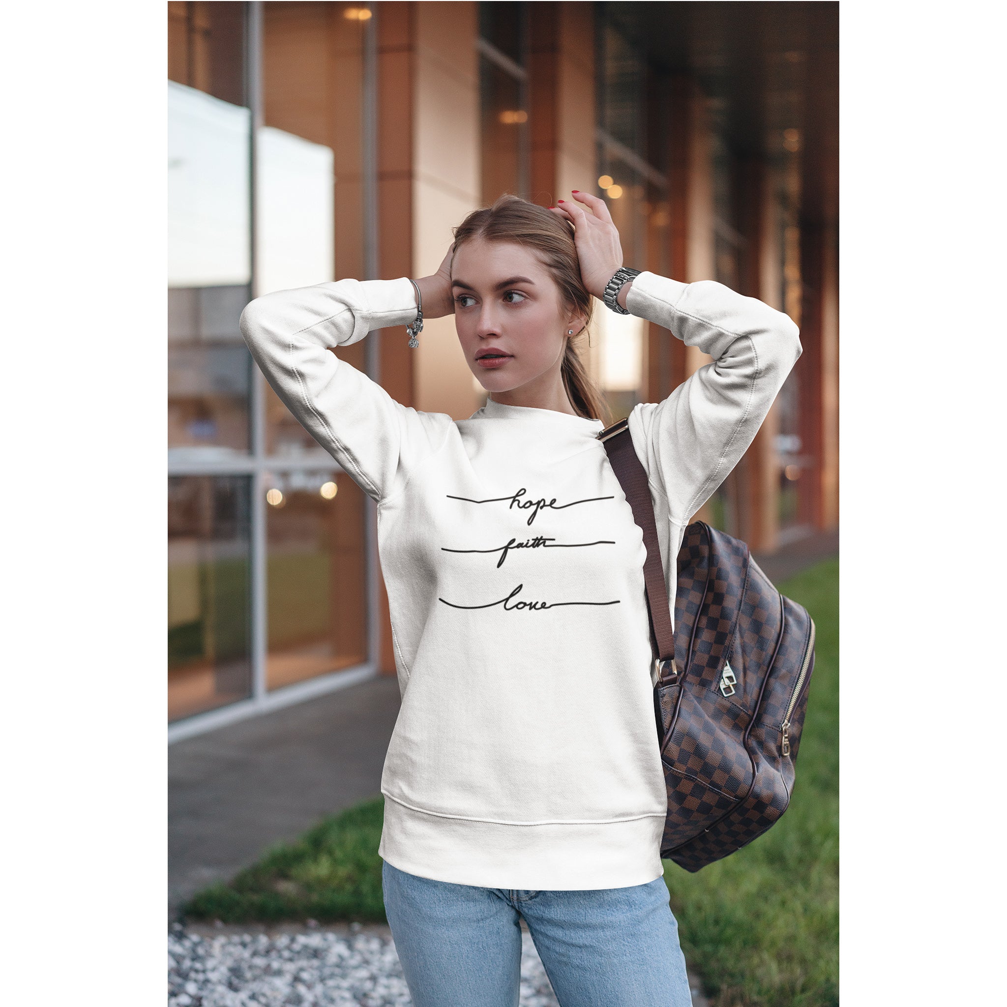 Woman wearing a white sweatshirt with text, standing outdoors.