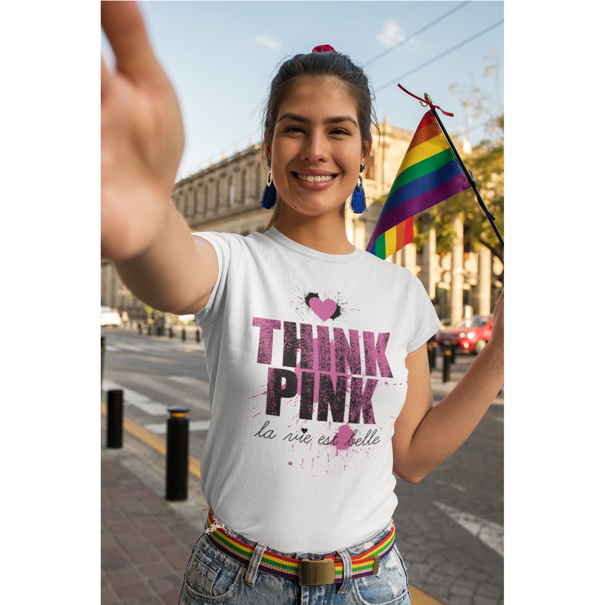 Person wearing a 'Think Pink' t-shirt with a rainbow flag in the background