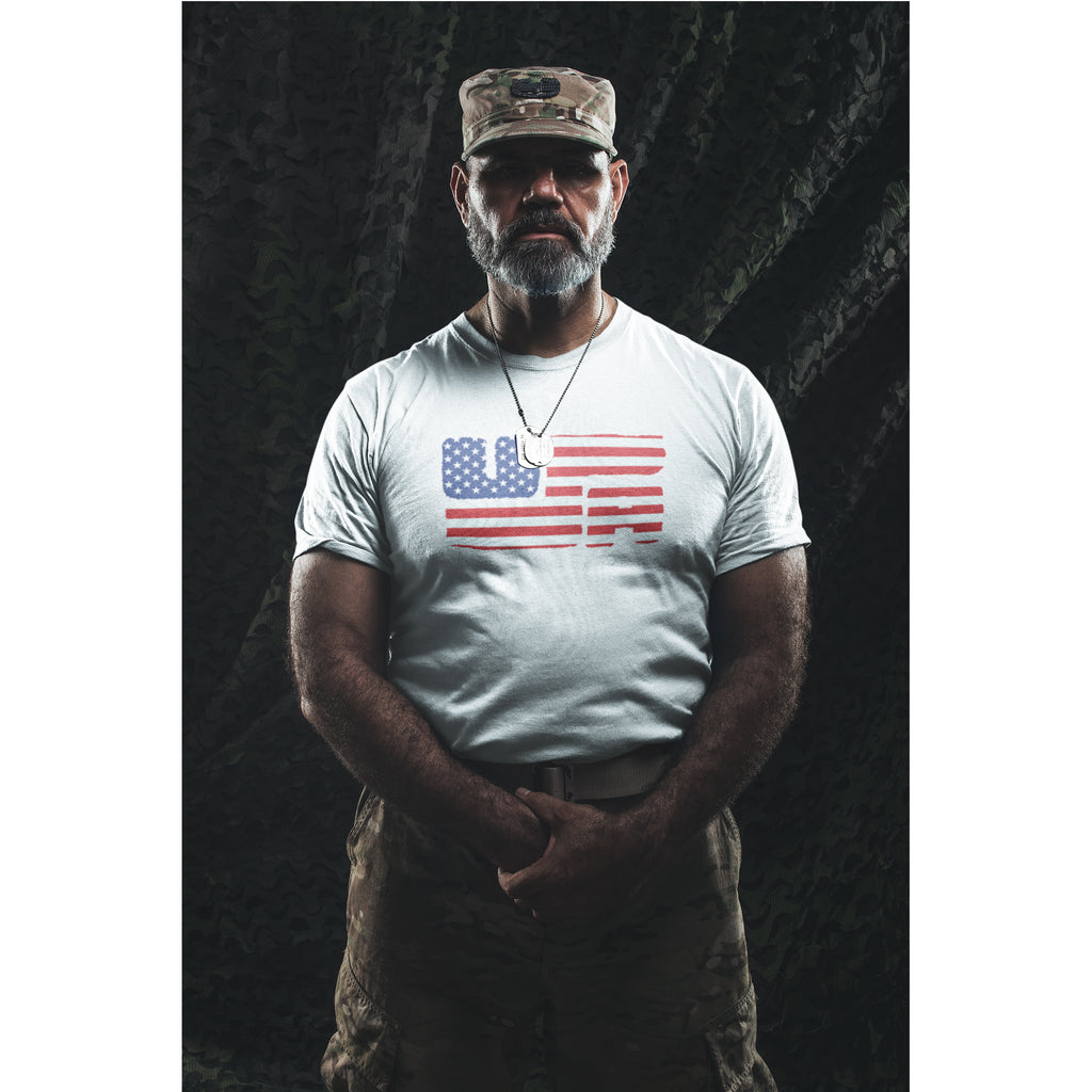 Man wearing a white t-shirt with an American flag design and a camouflage cap against a dark background.
