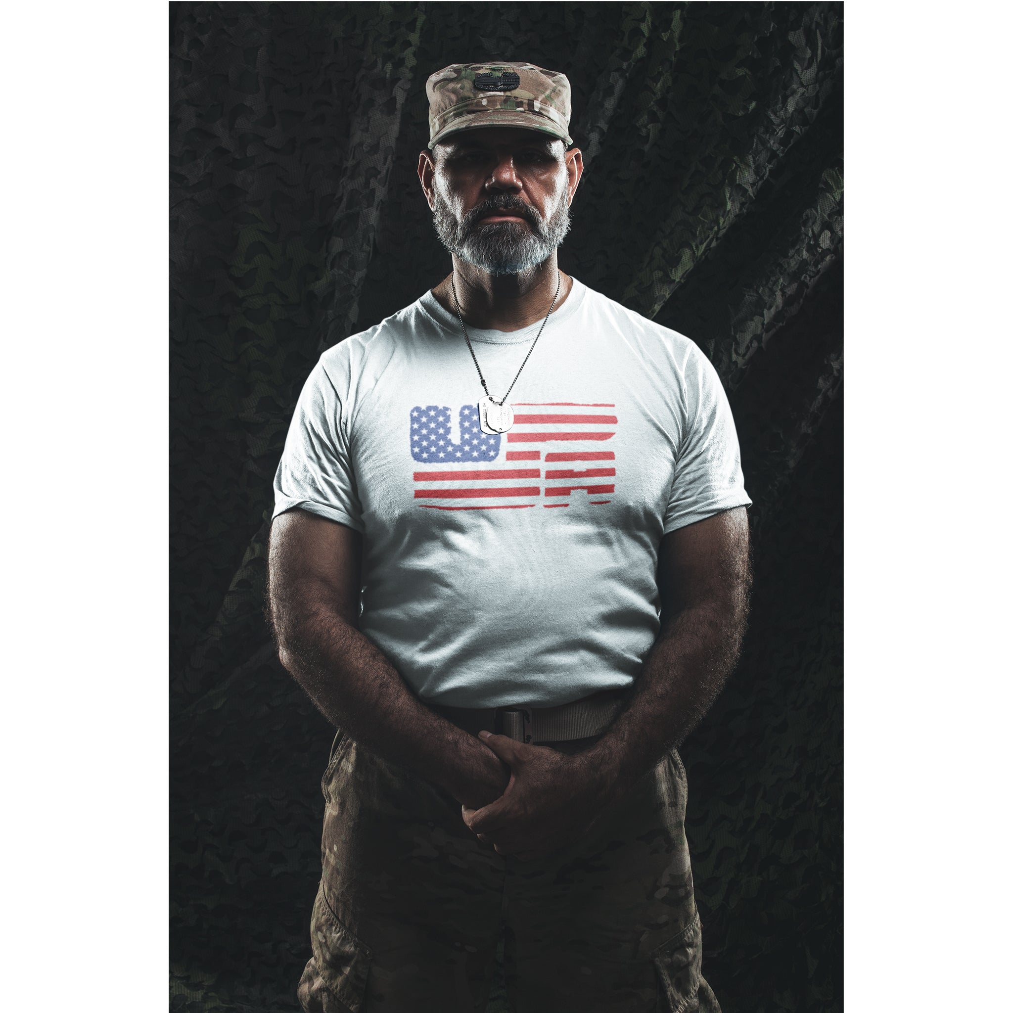 Man wearing a white t-shirt with an American flag design and a camouflage cap against a dark background.