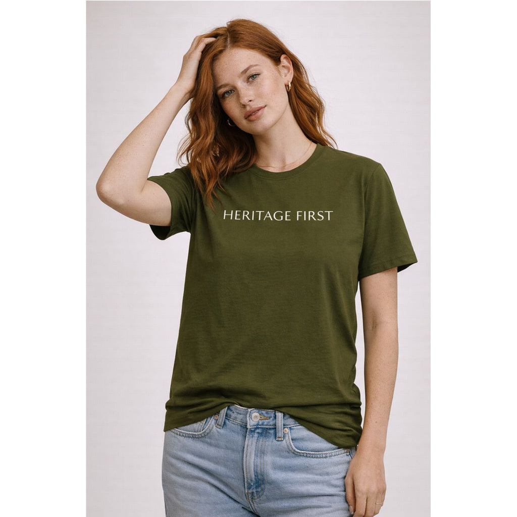 Woman wearing an olive green t-shirt with 'HERITAGE FIRST' text on a plain background