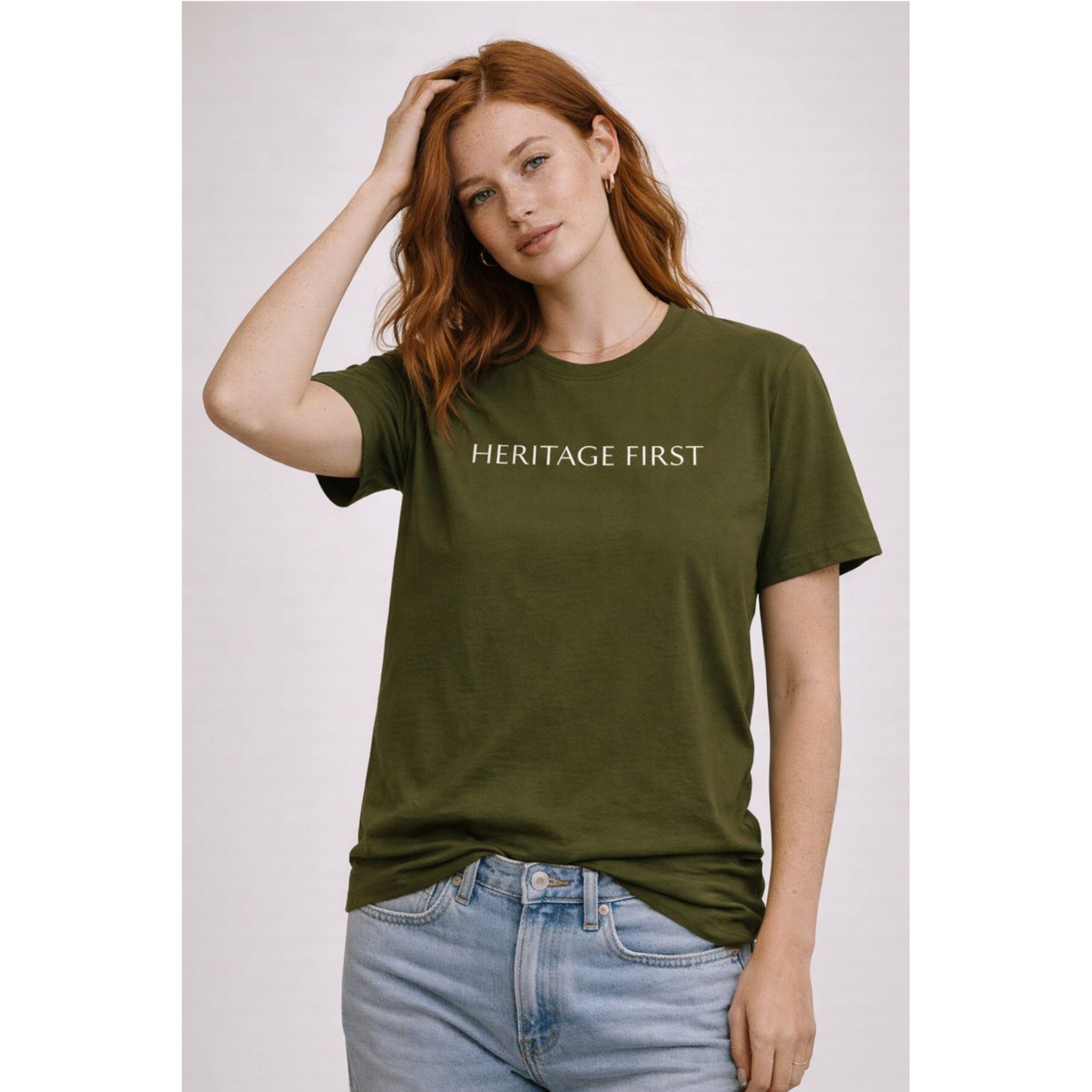 Woman wearing an olive green t-shirt with 'HERITAGE FIRST' text on a plain background