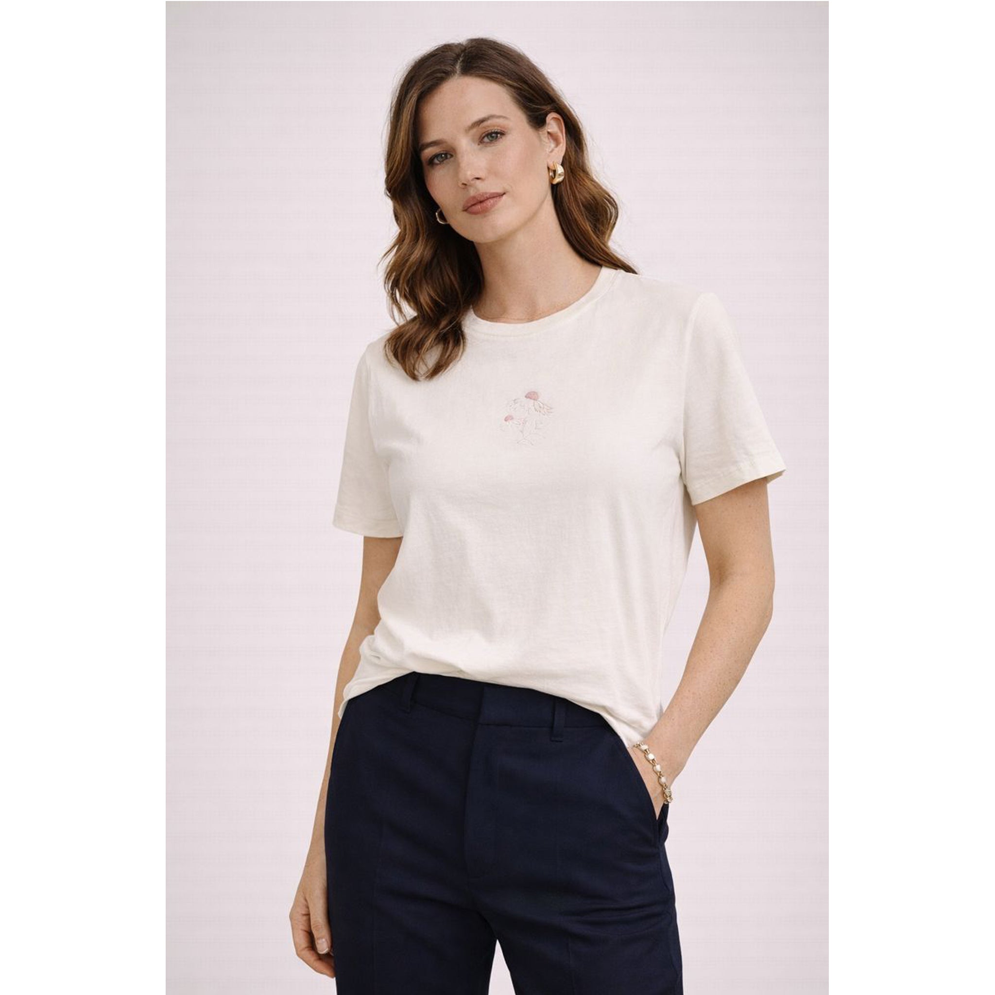 Woman wearing a white t-shirt and navy pants on a light pink background