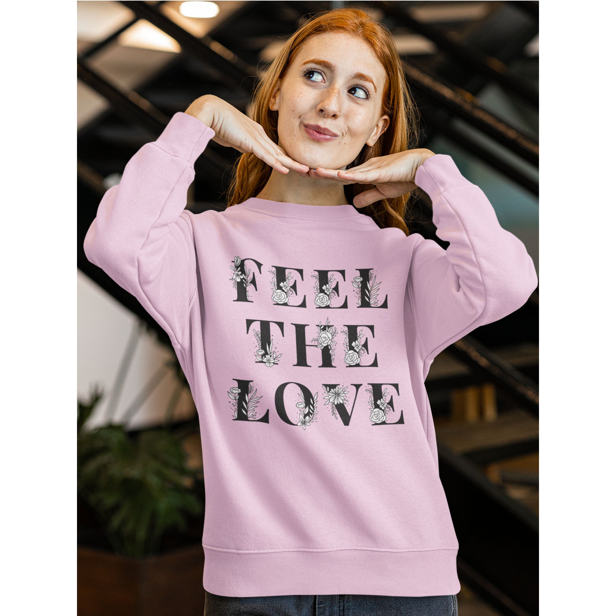 Person wearing a pink sweatshirt with 'FEEL THE LOVE' text and floral designs.