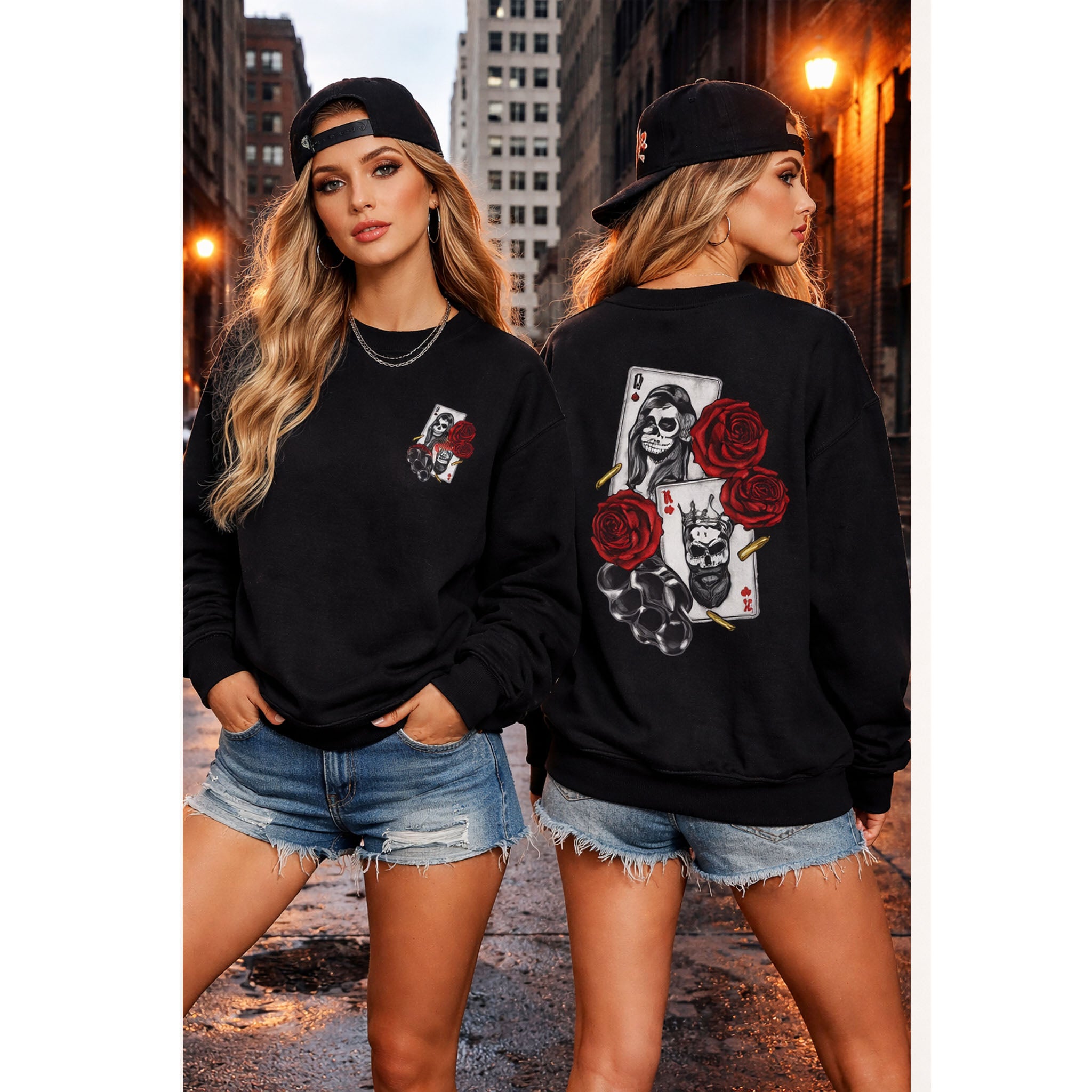 Two women wearing black sweatshirts with unique designs, one with roses and a skull, the other with playing cards and roses, in an urban setting.