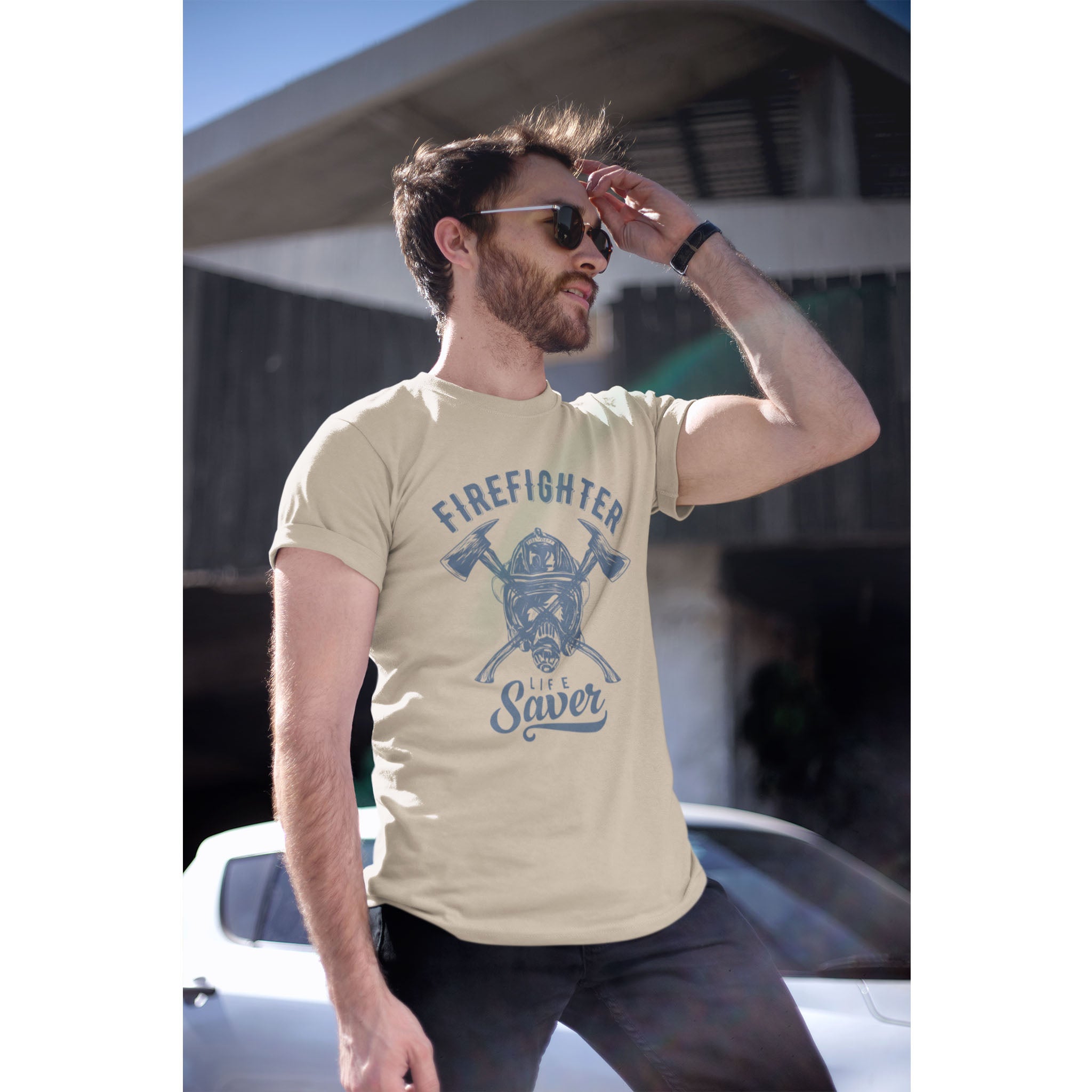 Man wearing a beige t-shirt with 'Firefighter Life Saver' graphic outdoors.