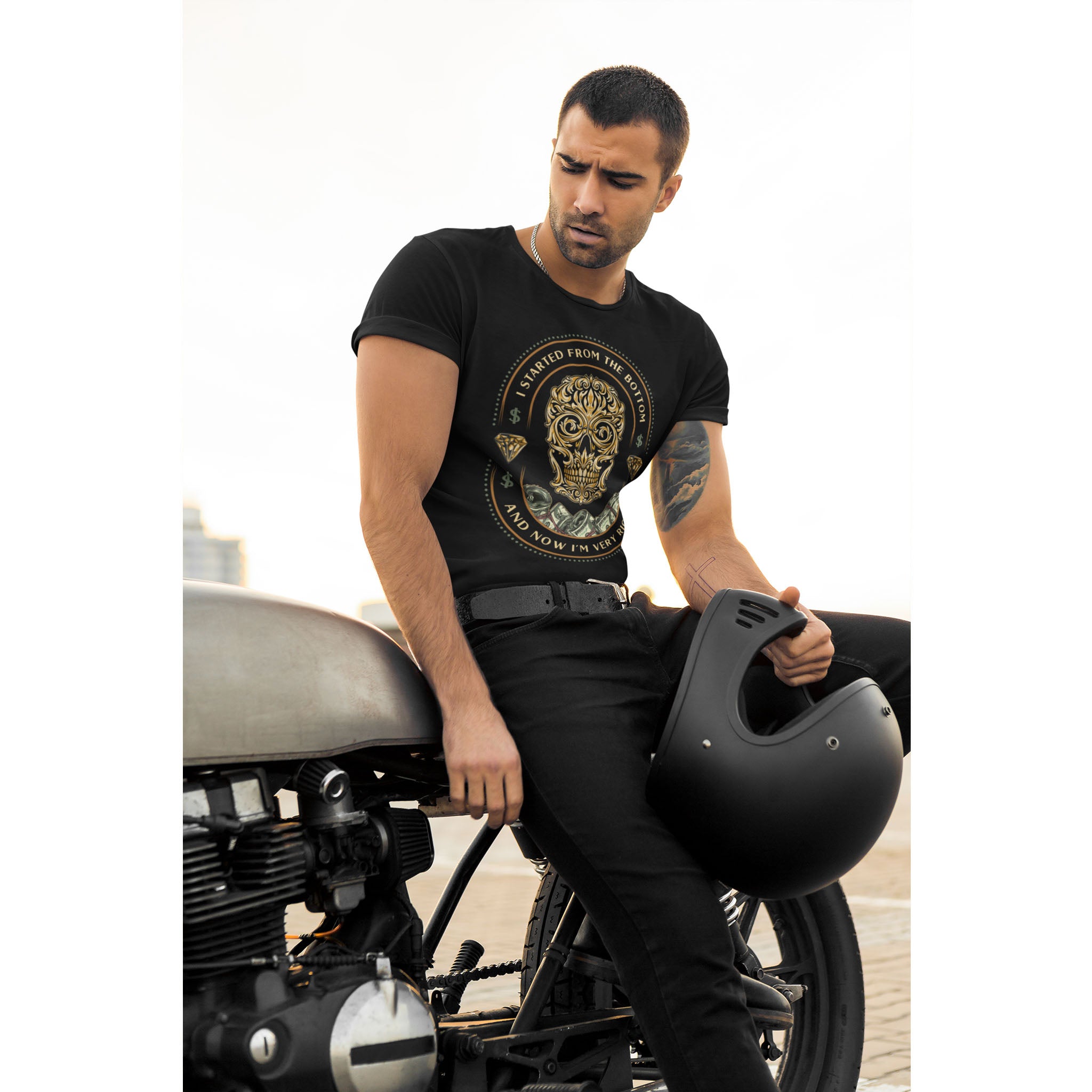 Man sitting on a motorcycle holding a helmet, wearing a black t-shirt with a graphic design.