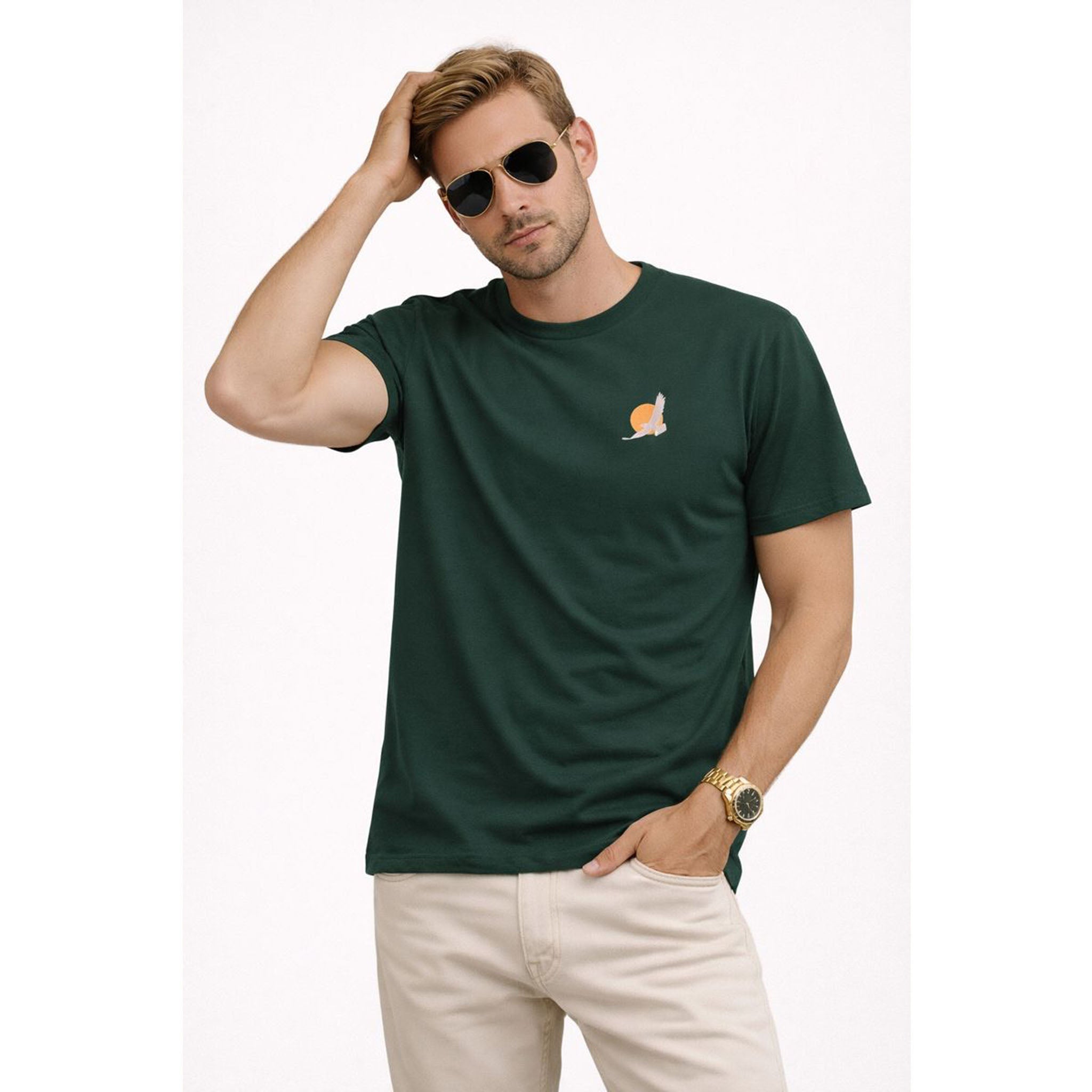 Man wearing a green t-shirt with a small logo, sunglasses, and beige pants on a white background – Bamerix