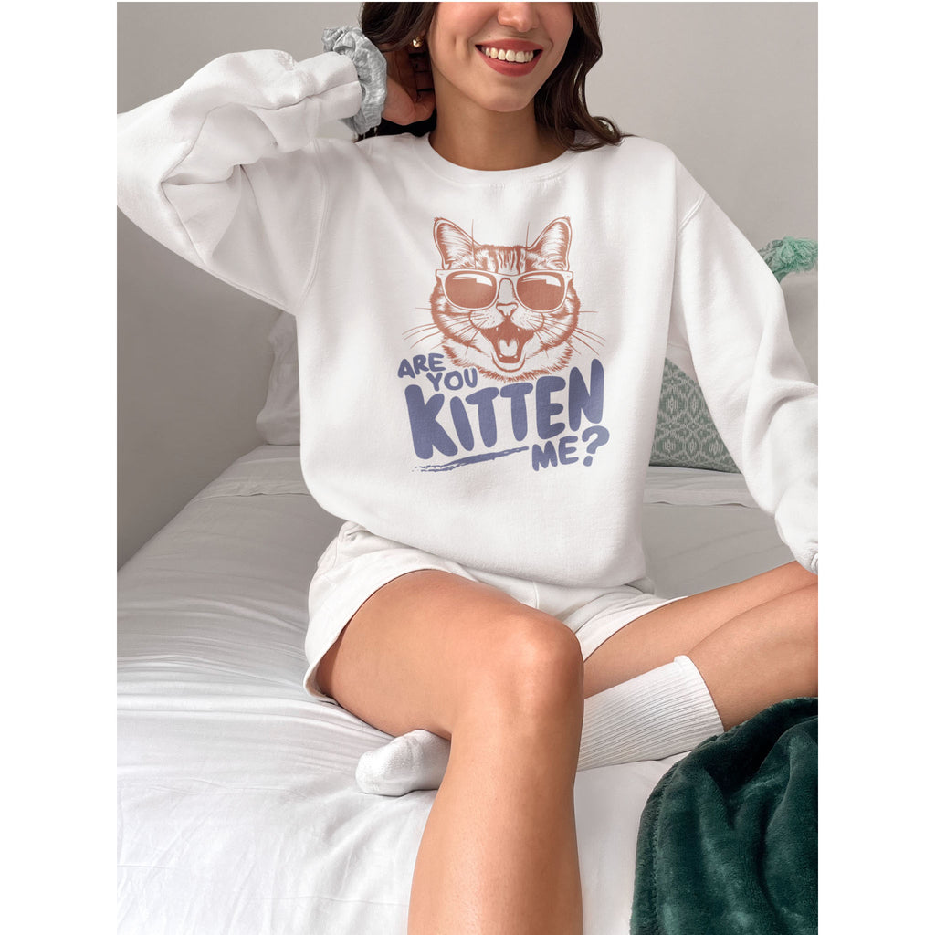 Person wearing a white sweatshirt with a cat graphic and text, sitting on a bed.