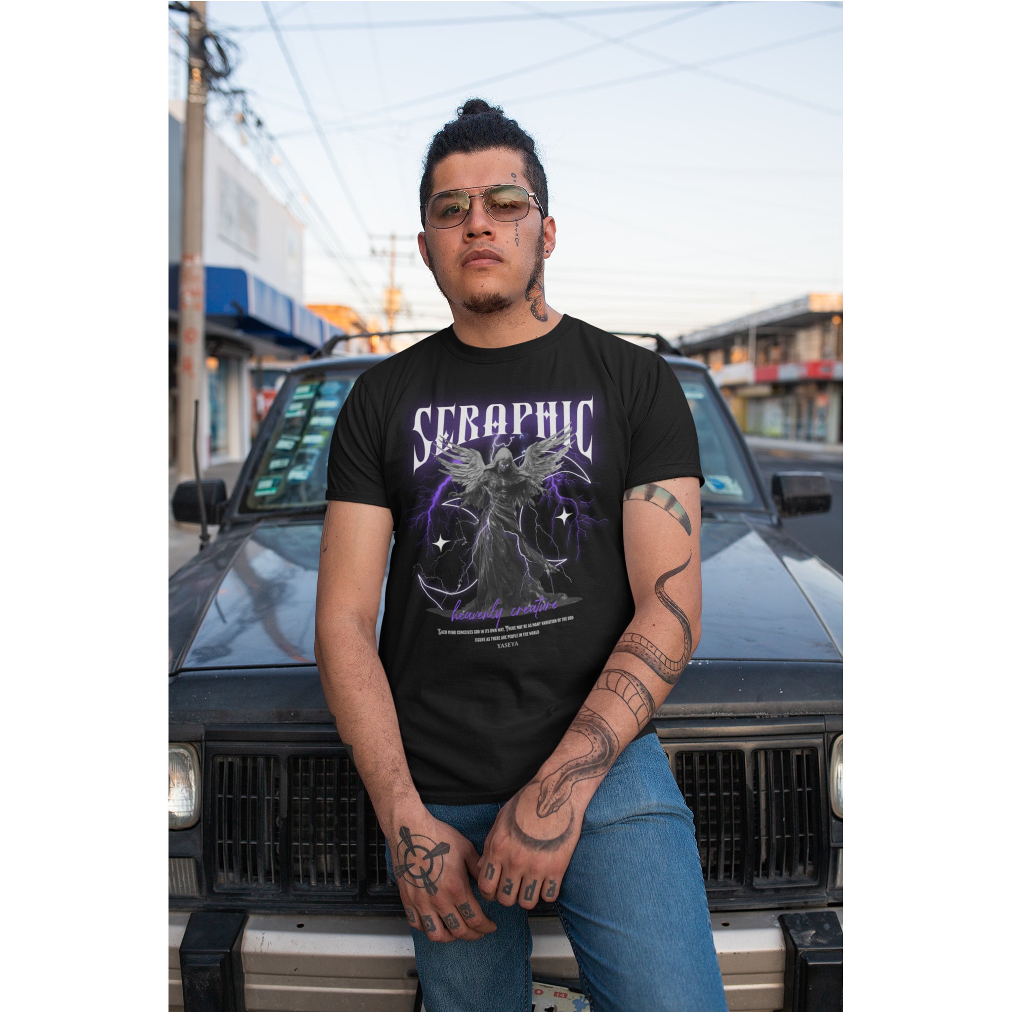 Person wearing a black t-shirt with a graphic design, standing in front of a vehicle.