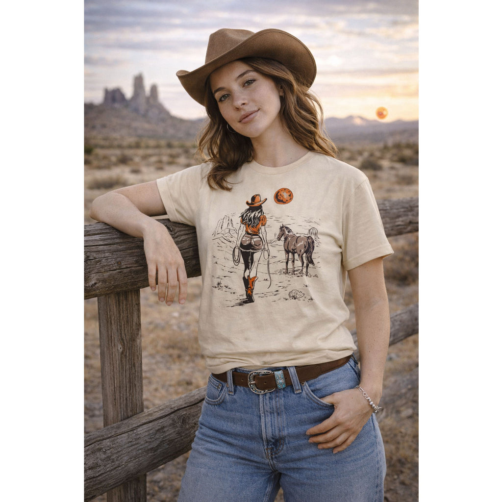 Woman wearing a t-shirt with a graphic design of a cowgirl and two dogs, standing in a desert landscape – Bamerix