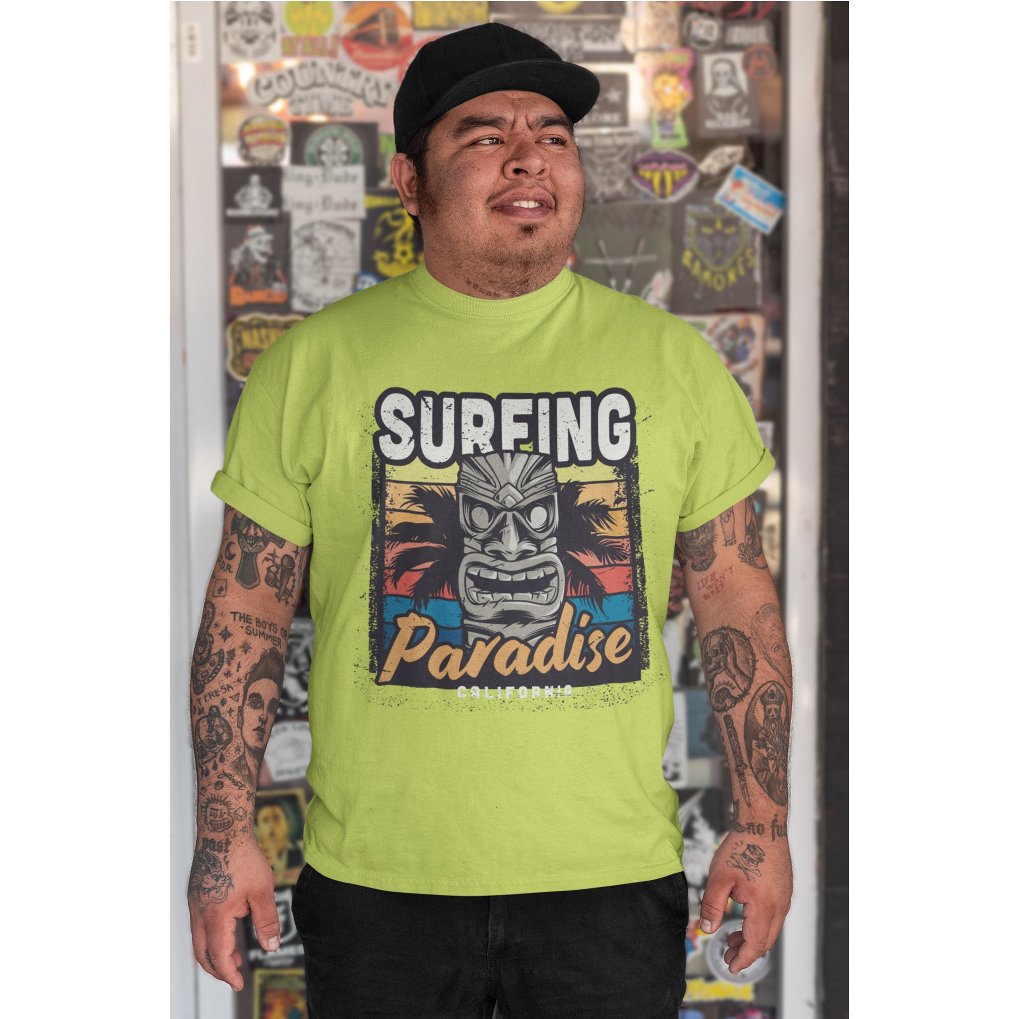 Person wearing a bright green t-shirt with 'Surfing Paradise' graphic design, standing in front of a wall with various posters.