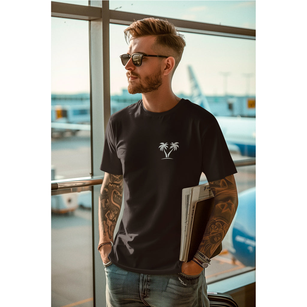 Man wearing a black t-shirt with a palm tree design, standing in an airport.