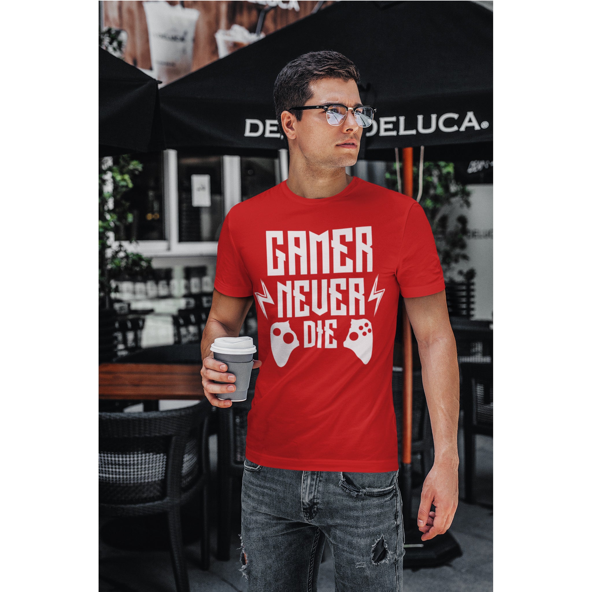 Man wearing a red t-shirt with 'Gamer Never Die' text and graphics, holding a coffee cup outdoors.