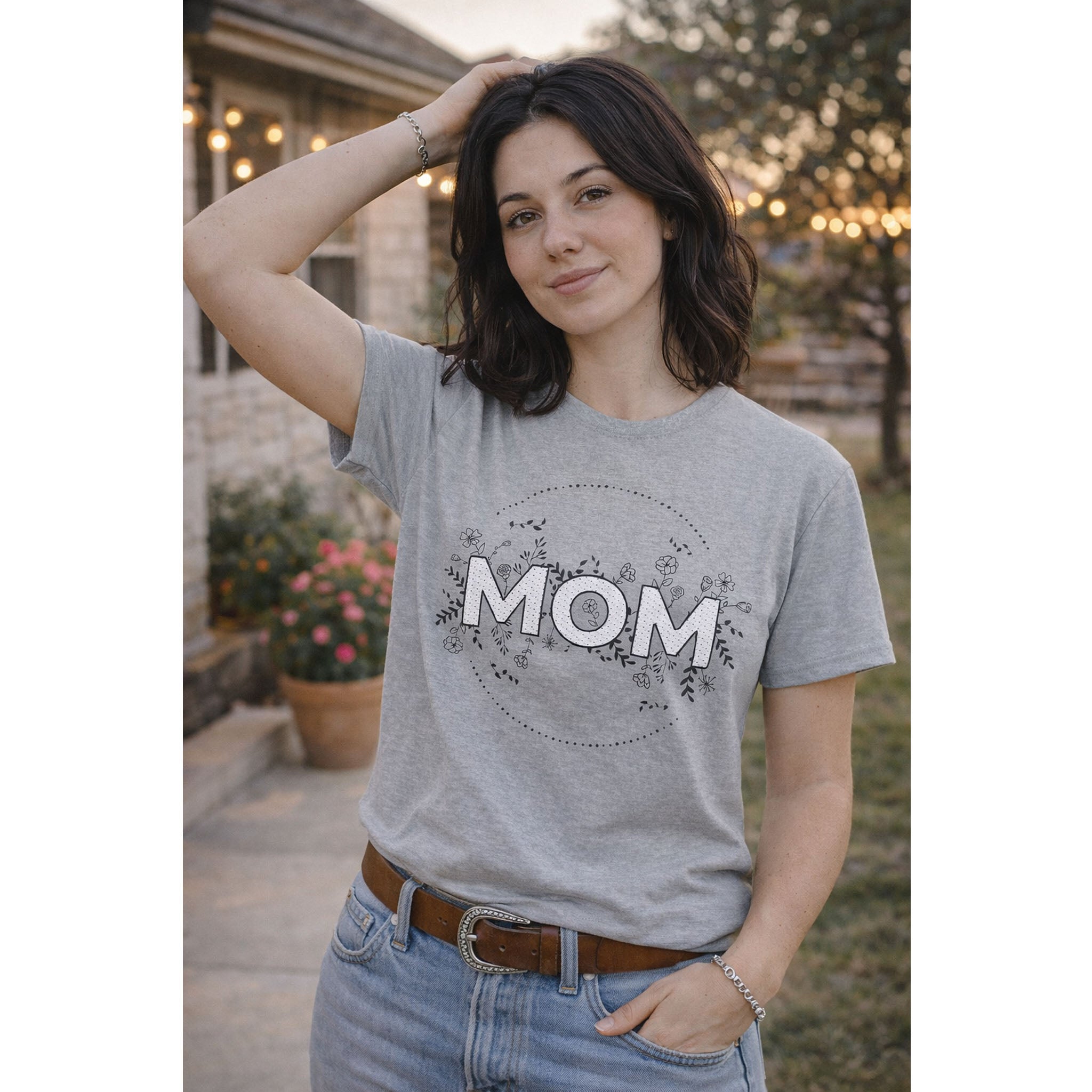 Woman wearing a gray t-shirt with 'MOM' printed on it, standing outdoors.