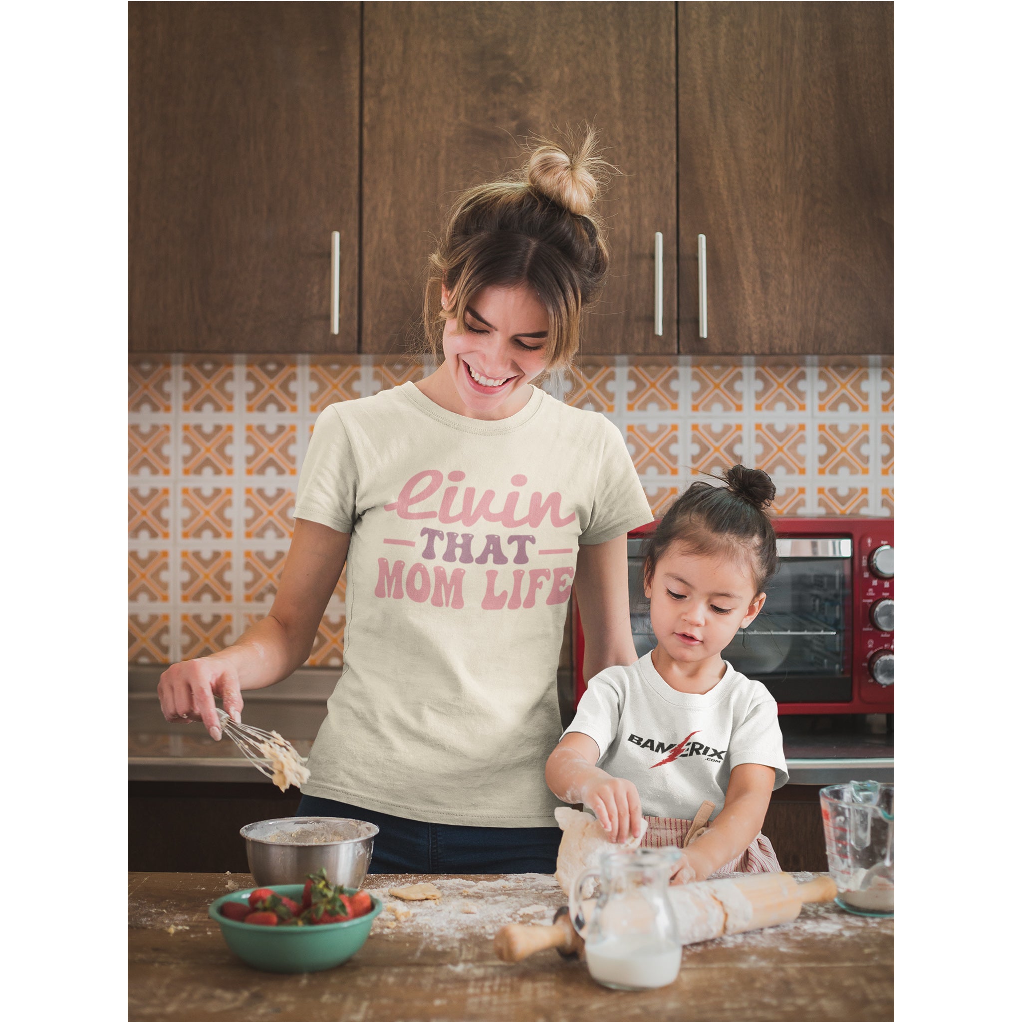 Woman and child in a kitchen with a woman wearing a 'Livin That Mom Life' shirt.