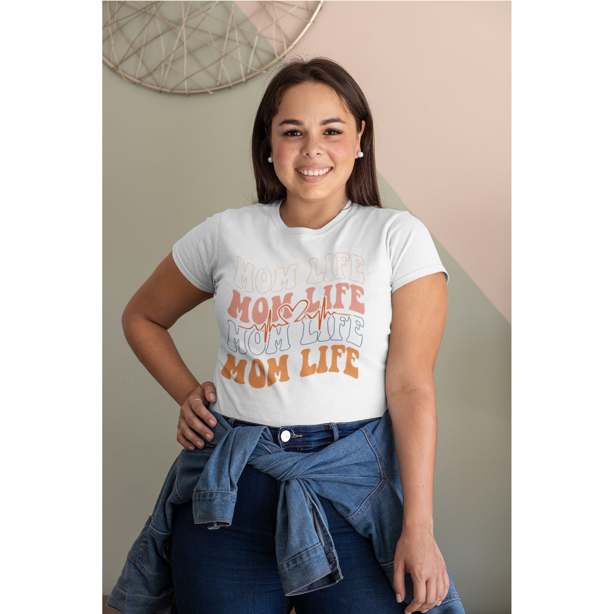 Woman wearing a white t-shirt with 'Mom Life' text, standing against a neutral wall.
