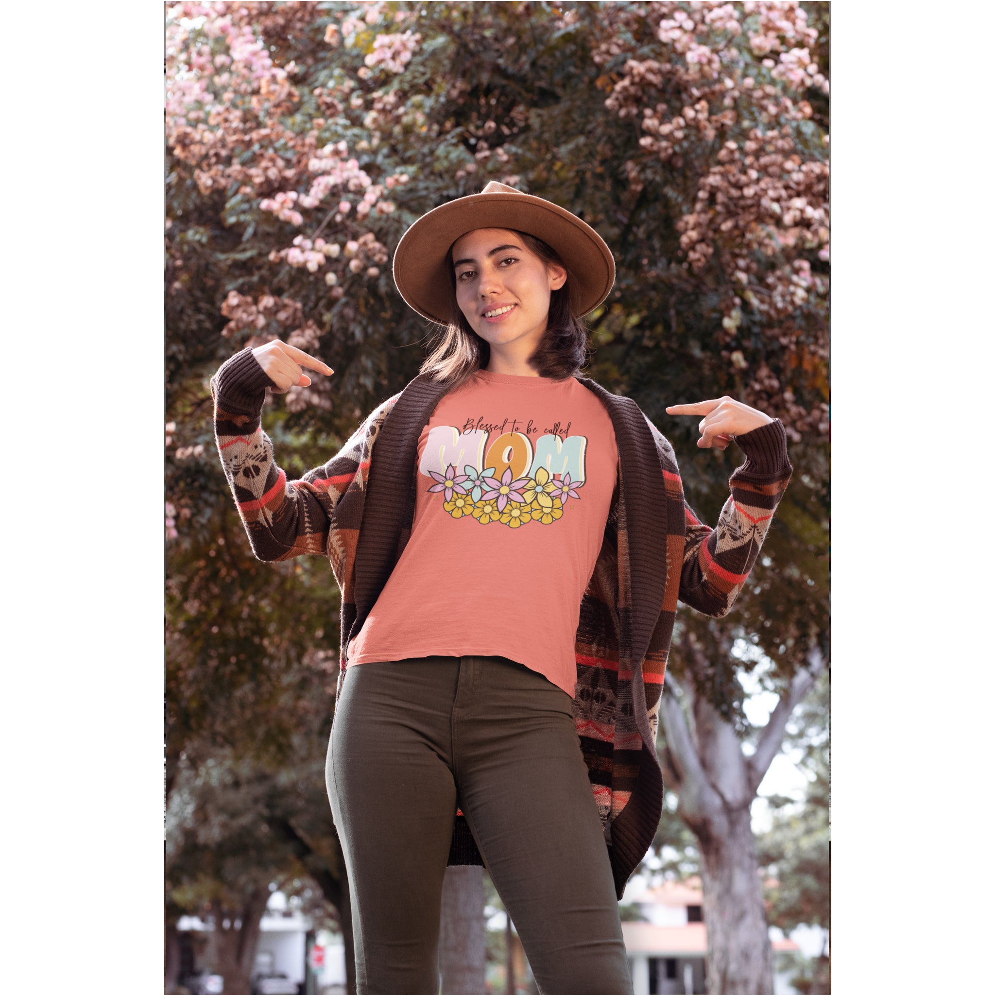 Woman wearing a pink t-shirt with a graphic design, brown cardigan, and hat outdoors – Bamerix