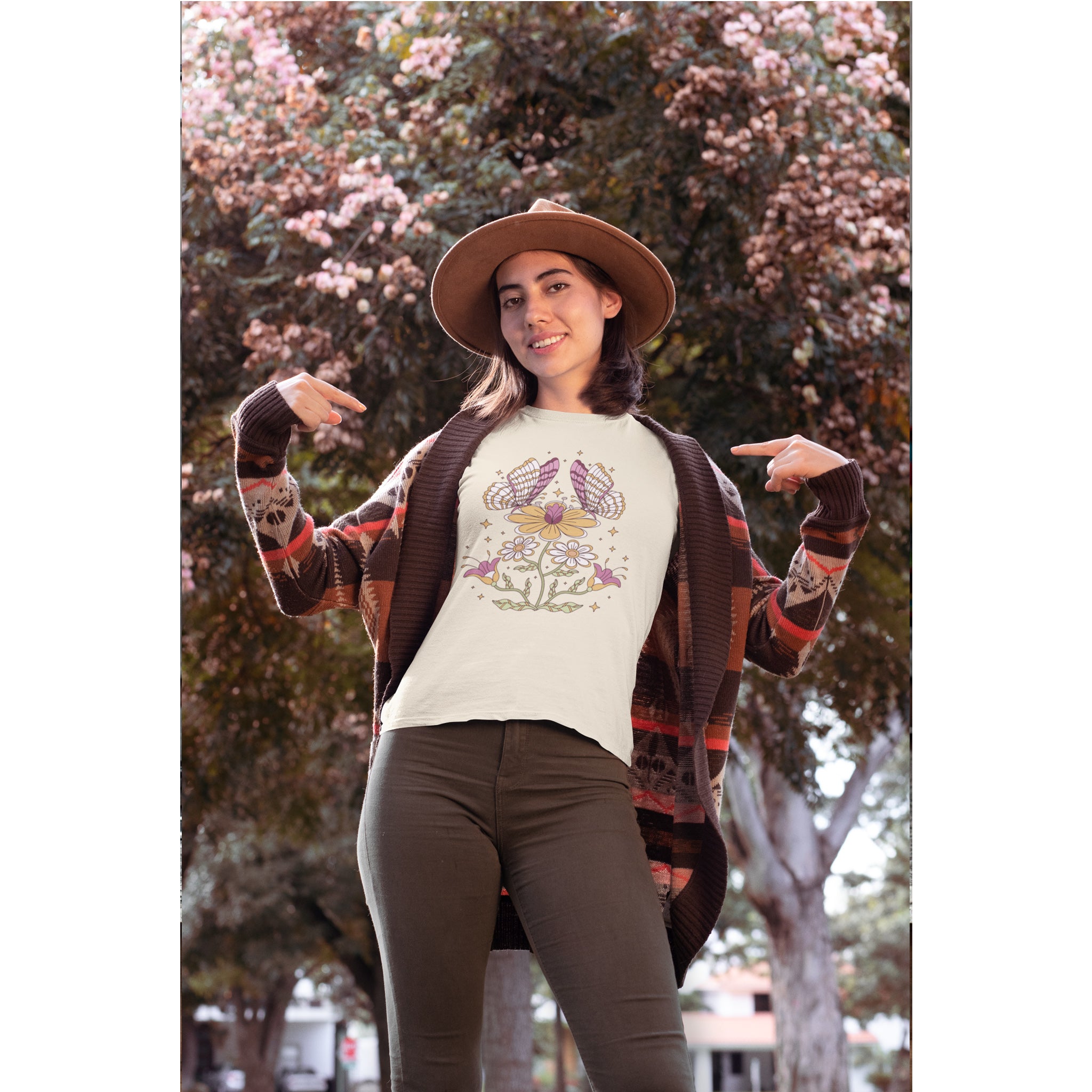 Woman wearing a patterned cardigan, beige shirt with graphic design, and brown pants outdoors.