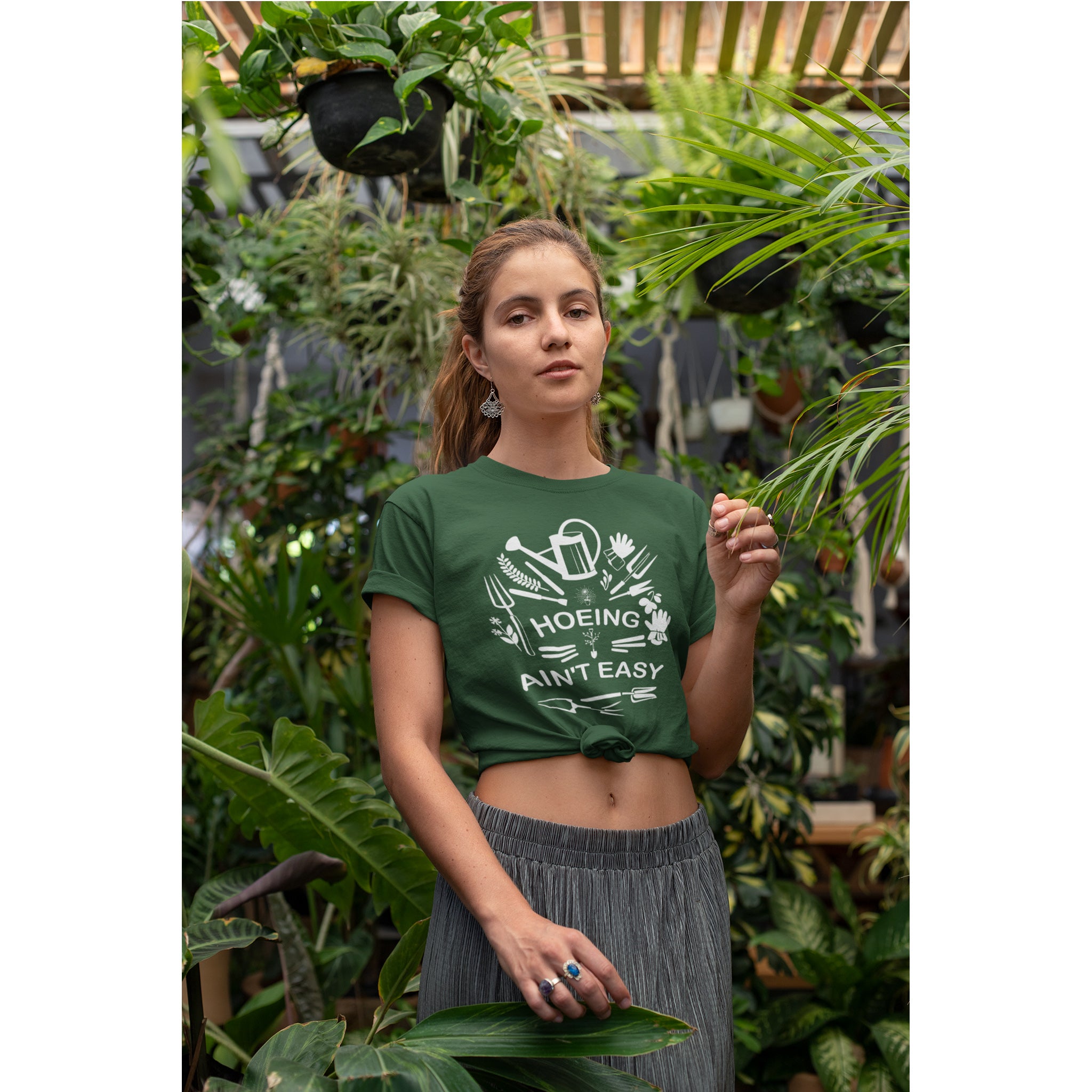 Woman wearing a green t-shirt with a graphic design and text, standing in a garden setting.