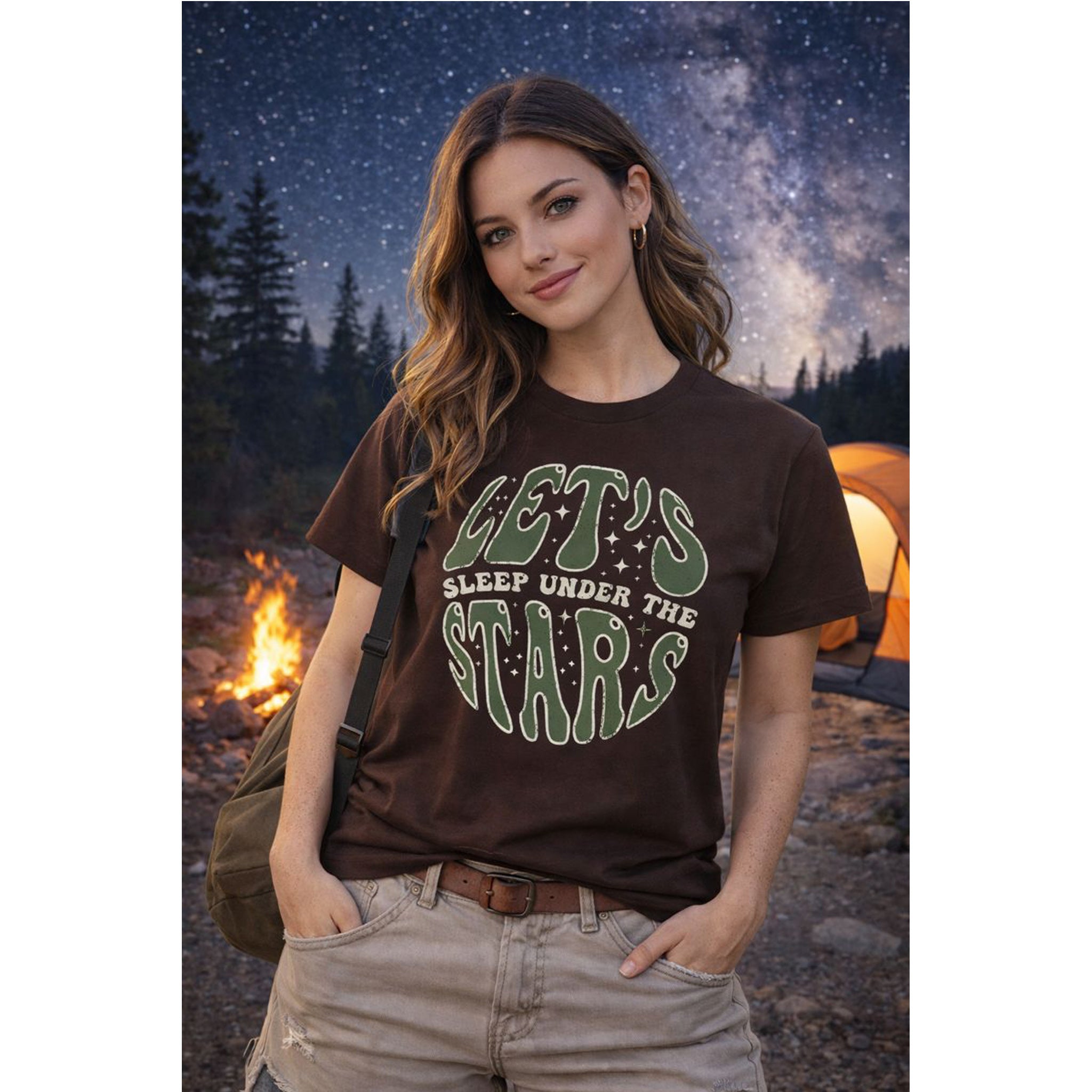 Woman wearing a 'Let's Sleep Under the Stars' t-shirt in a camping setting with a tent and fire.