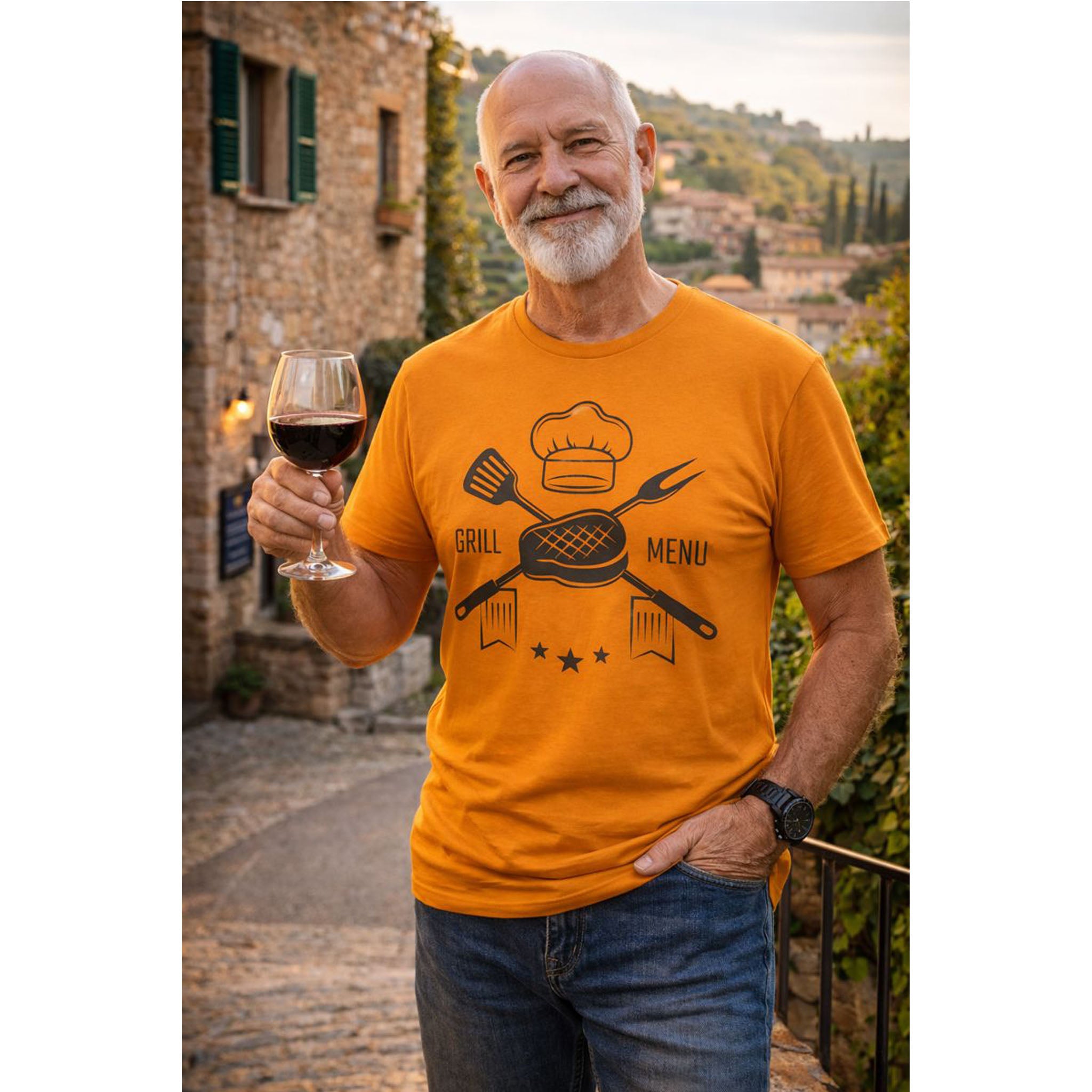 Man wearing an orange t-shirt with a graphic design, holding a glass of wine in a scenic outdoor setting.