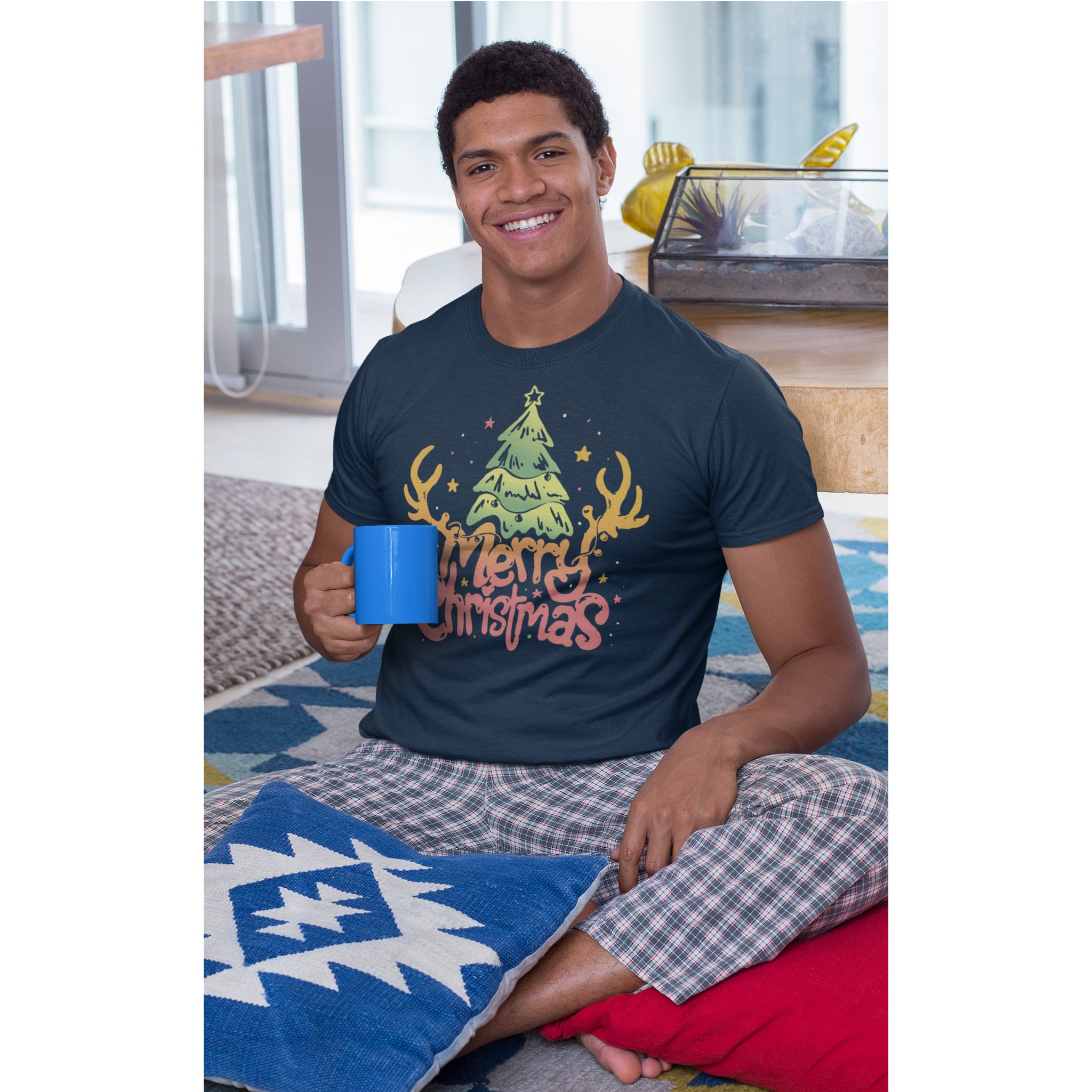 Man wearing a Christmas-themed t-shirt and holding a mug, sitting on a bed.