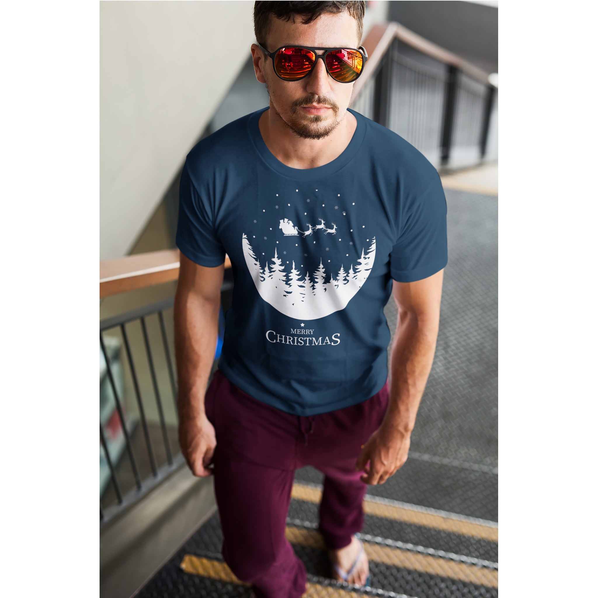 Man wearing a navy blue t-shirt with a Christmas design, standing on a staircase.