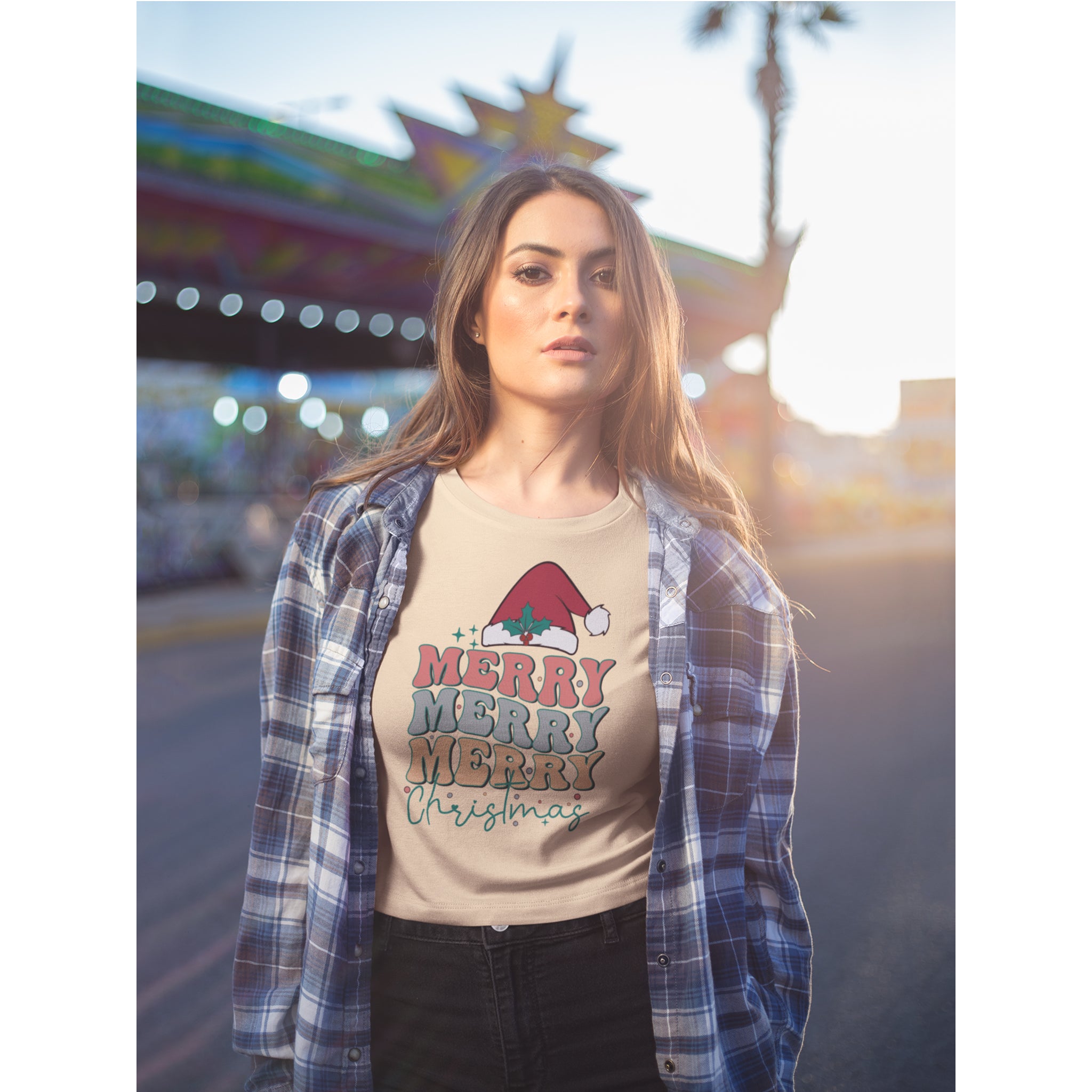 Woman wearing a 'Merry Merry Christmas' t-shirt with a plaid shirt in a festive outdoor setting.